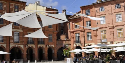Le Pignié courtyard in Lescure-d'Albigeois with terracotta buildings, white shade sails, and outdoor dining area.