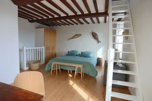 Chambre de charme rustique avec poutres apparentes, literie bleu-canard, mobilier en bois et escalier blanc vers la mezzanine
