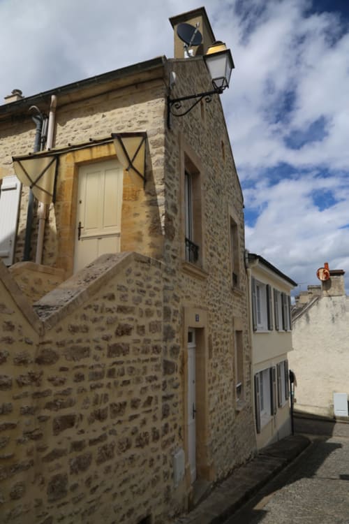 Façade du gîte en pierre aux Filles du Bord de Mer à Port-en-Bessin avec porte crème et vue sur la rue
