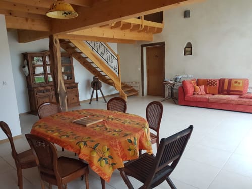 Spacieuse salle à manger de la Ferme Passion B&B avec nappe orange, poutres en bois et canapé rouge en arrière-plan