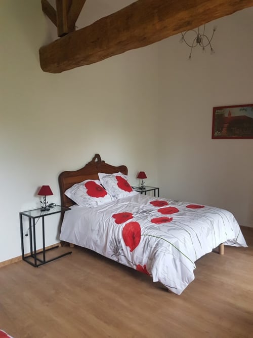 Chambre accueillante à la Ferme Passion B&B avec poutre en bois, literie aux coquelicots rouges et charme rustique à Saint-Trivier-sur-Moignans