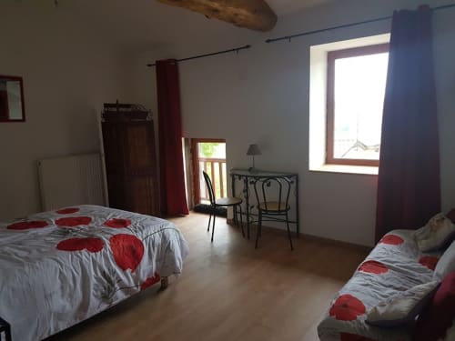 Chambre spacieuse à la Ferme Passion B&B avec literie à motifs rouges, poutres apparentes et grandes fenêtres avec vue