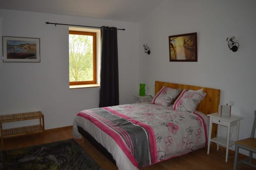 Chambre lumineuse à la Ferme Passion B&B avec parure florale rose, lit en bois et vue sur le jardin verdoyant