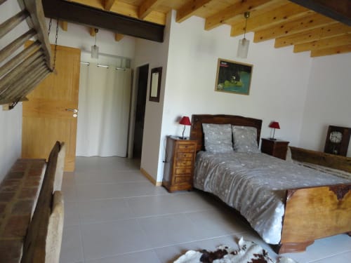 Chambre spacieuse à la Ferme Passion B&B avec poutres en bois, lit double, tables de nuit avec lampes rouges et décor rustique