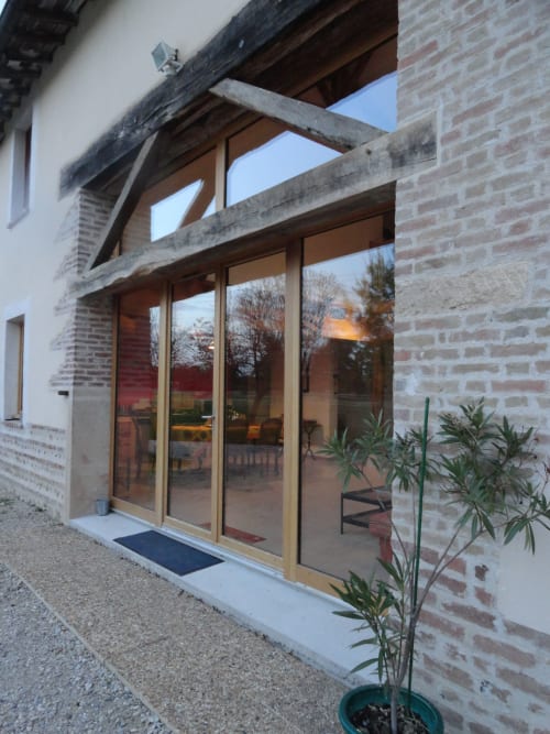 Portes et fenêtres modernes en verre à l'entrée de la Ferme Passion B&B, Saint-Trivier-sur-Moignans, avec façade en brique et poutres en bois.