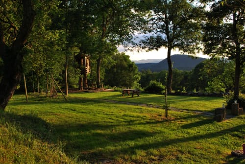 Jardin verdoyant avec tables de pique-nique, arbres centenaires et montagnes au loin, gîte Aux Pays Des Sucs, Saint-Hostien