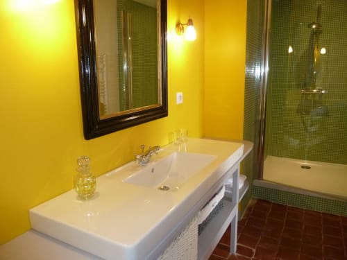Baño moderno en el Château De Clusors con paredes amarillo brillante, lavamanos blanco, ducha de azulejos verdes y espejo con marco negro