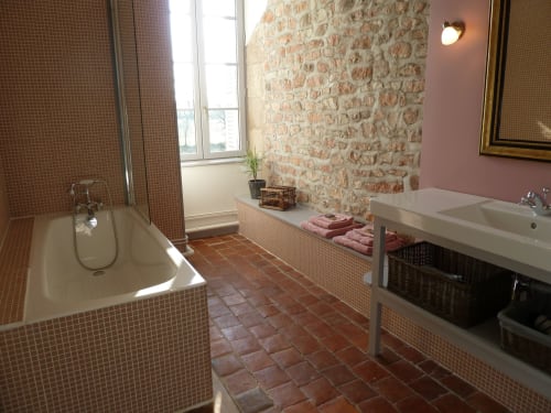 Salle de bain spacieuse de la chambre Lilas au Château De Clusors avec carrelage terracotta, mur en brique, baignoire et lavabo