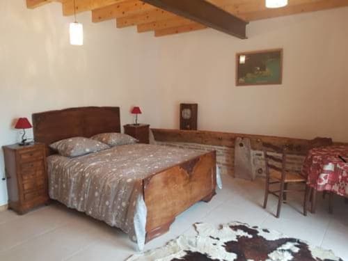 Chambre spacieuse à Ferme Passion avec poutres en bois, lit double, tables de nuit aux lampes rouges et tapis en peau de vache