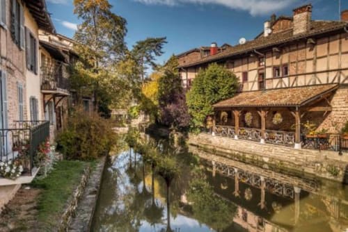 Village médiéval au bord de l'eau avec bâtiments en pierre et structures en bois se reflétant dans une eau calme à Ferme Passion