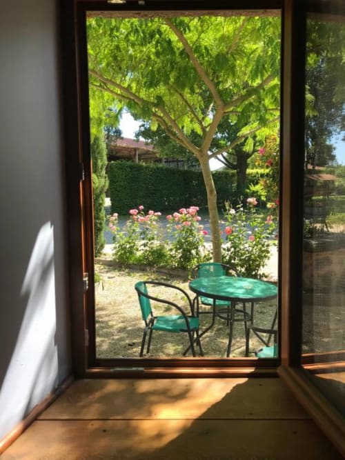 Vue du jardin de la chambre La Raymondière avec table verte, chaises, roses en fleur et arbres d'ombrage à Vernoux-en-Gâtine
