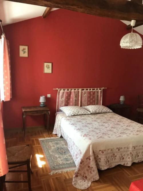 Chambre triple accueillante à La Raymondière avec murs rouges, literie fleurie et vue sur le jardin à Vernoux-en-Gâtine