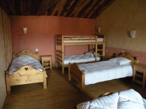 Chambre rustique avec lits en bois, murs rouges et plafond à poutres à La Raymondière à Vernoux-en-Gâtine