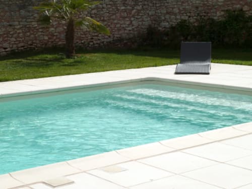 Turquoise swimming pool at Château De Clusors B&B in Saint-Ménoux, France, with stone walls and lounge chair