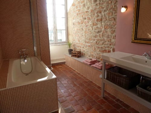 Amplio cuarto de baño en el Château De Clusors con paredes de ladrillo, azulejos de terracota, bañera y lavamanos en Saint-Menoux