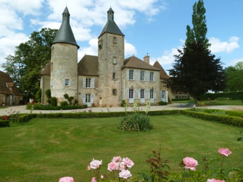 Château de Clusors, mansión histórica de piedra con torres gemelas y rosas rosadas en el jardín, Saint-Menoux Francia