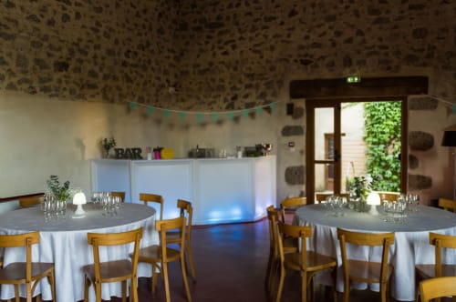 Salle d'événements à La Raymondière avec tables rondes, chaises en bois et plafond en pierre