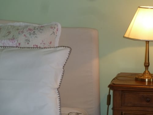 Detalle de dormitorio en el Château de Clusors con almohada floral, funda blanca con ribete y lámpara de mesa de latón en la habitación Montespan