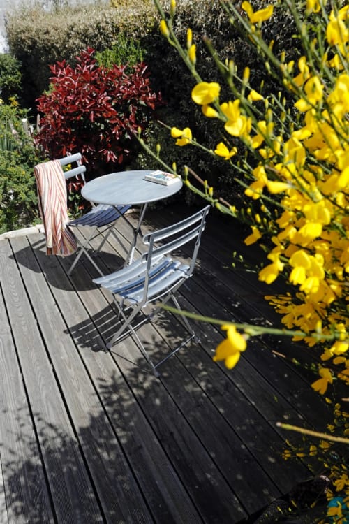 Terrasse ensoleillée de Côte Et Dune avec table ronde, chaises et fleurs jaunes dominant le jardin