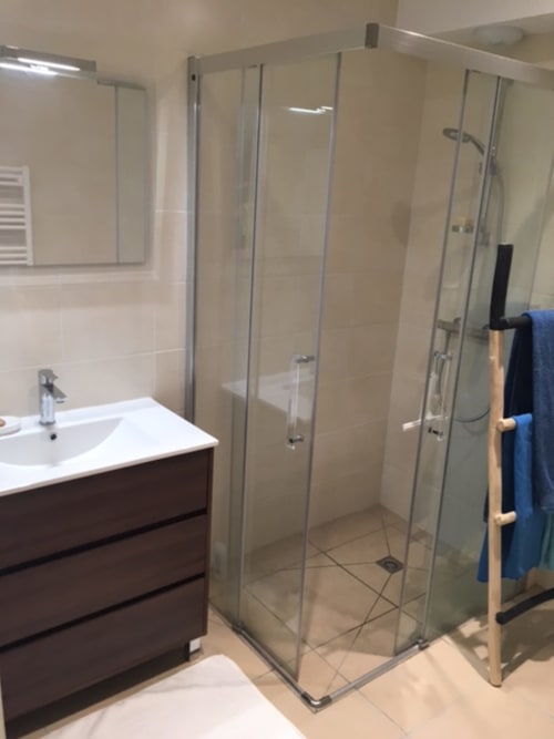 Salle de bain moderne avec douche d'angle vitrée, vasque blanche et porte-serviettes en bois à l'appartement Côte Et Dune,