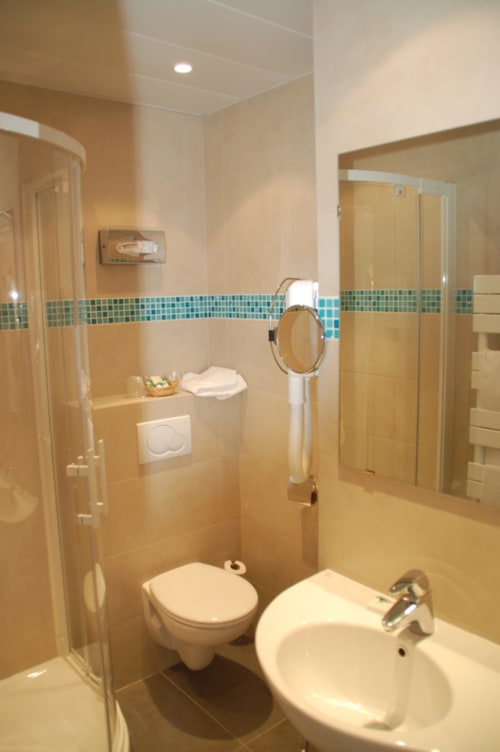 Moderno bagno dell'hotel Nice con piastrelle beige, fascia turchese, doccia, wc, lavabo e specchio
