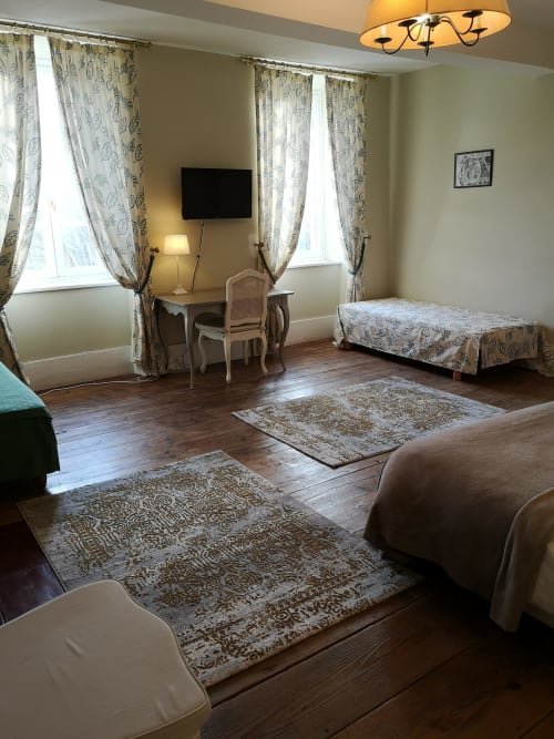 Chambre beige spacieuse à la maison d'hôtes L'affable aux Cammazes avec lits multiples, rideaux à motifs et parquet ancien