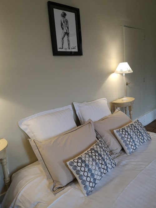 Chambre beige confortable de la maison d'hôtes L'affable aux Cammazes avec oreillers blancs, coussins à motifs, lampe de chevet et tableaux encadrés