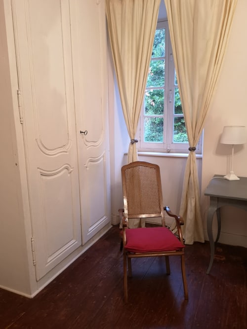 Chambre élégante à L'affable B&B aux Cammazes avec fauteuil en rotin, coussin rouge et grandes fenêtres