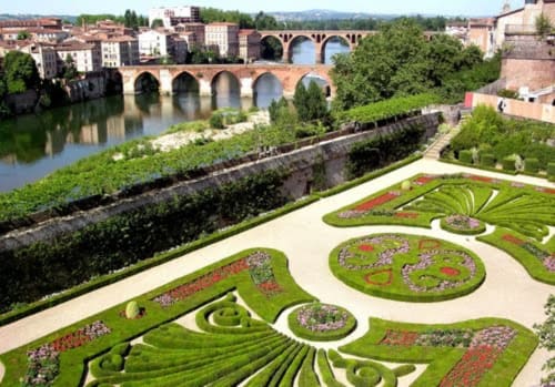 Jardin formel aux haies ornementales et parterres de fleurs dominant un pont en arc et la rivière aux Cammazes, France