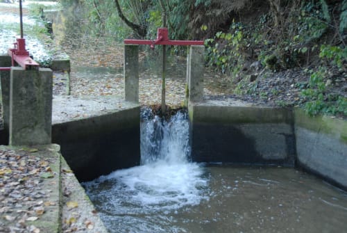 L'eau s'écoule à travers la porte métallique rouge du moulin d'Ajon à Maisoncelles-sur-Ajon, France