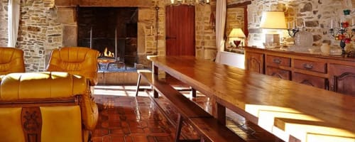 Intérieur chaleureux et rustique du gîte Le Moulin d'Ajon avec sièges en cuir doré, table en bois et murs en pierre