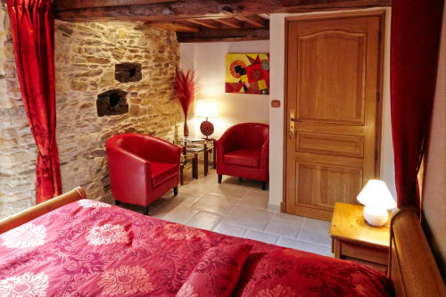 Chambre luxueuse du Moulin d'Ajon avec lit à motifs roses, fauteuils rouges, murs en pierre et porte en bois à Maisoncelles