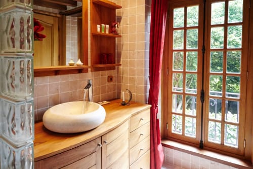 Salle de bains élégante avec vasque blanche, meuble bois, étagères rouges et portes-fenêtres donnant sur le jardin du Moulin d'Ajon