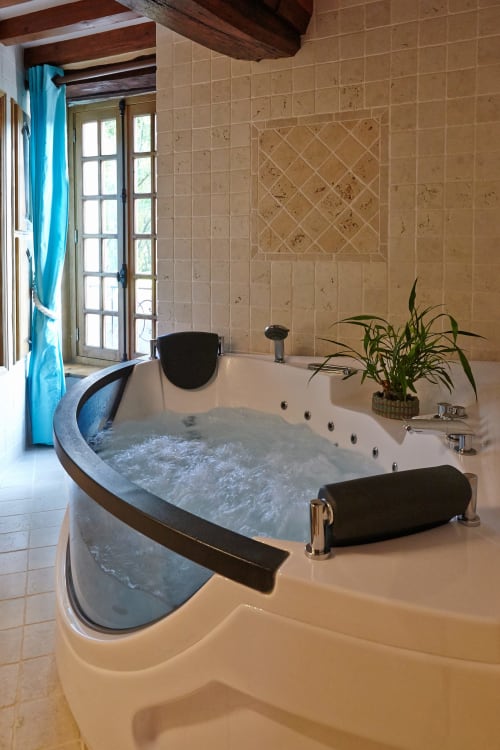 Baignoire de luxe avec jets et appuie-têtes noirs dans la Chambre du Meunier du Moulin d'Ajon, vue sur les jardins