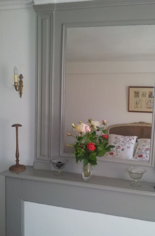 Chambre Charlotte au Domaine De Puyrousse avec fleurs fraîches sur la commode et miroir reflétant le lit aux oreillers fleuris