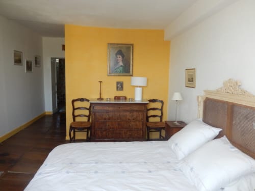 Chambre Marie au Domaine de Puyrousse : lit blanc, commode en bois, mur d'accent jaune et mobilier d'époque.