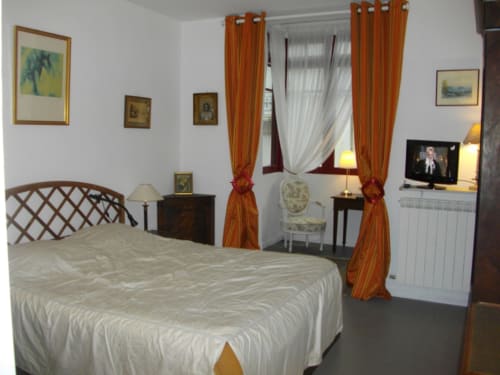Élégante chambre au Domaine De Puyrousse B&B à Villetoureix avec lit à baldaquin, rideaux orangés et décor classique