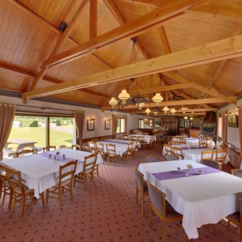 Salle à manger lumineuse à La Ferme Du Grand Air avec poutres en bois, tables blanches et touches violettes à Fiennes.