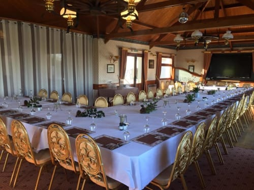Élégante salle de banquet à La Ferme Du Grand Air avec tables ornées, chaises raffinées et plafond aux poutres apparentes à Fiennes