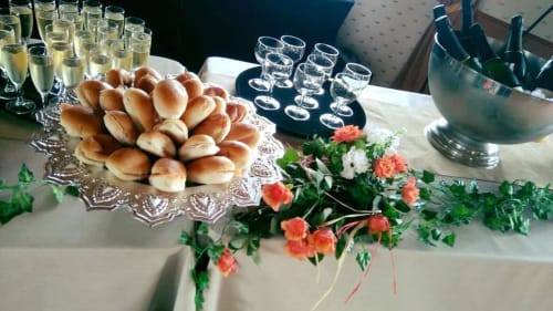 Élégante mise en table à La Ferme Du Grand Air : petits pains, champagne, vin et fleurs corail sur lin blanc.