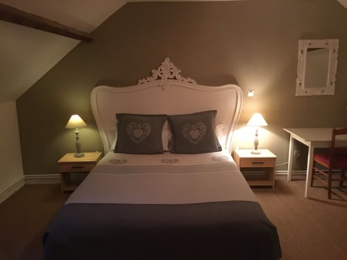Chambre élégante à La Ferme Du Grand Air avec tête de lit blanche ornée, oreillers foncés, lampes de chevet et jardin