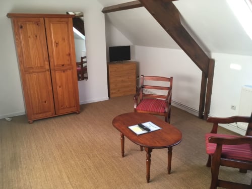 Chambre mansardée à La Ferme Du Grand Air avec mobilier en bois, télévision, chaises rouges et table ovale à Fiennes, France