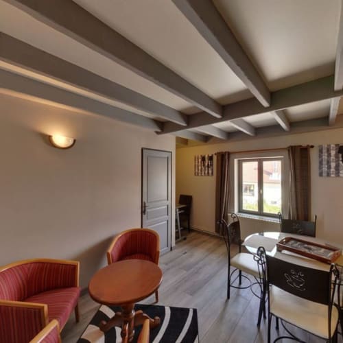 Spacieux séjour de chaumière à La Ferme Du Grand Air avec poutres apparentes, chaises rouges, table en bois et vue sur le jardin