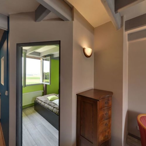 Couloir de chaumière moderne à La Ferme Du Grand Air avec buffet en bois, applique murale et porte ouverte révélant une chambre avec jardin