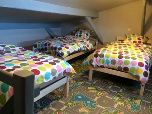 Literie colorée à pois dans une chambre rustique avec trois lits et sol thématique urbain à La Ferme Du Grand Air, Fiennes