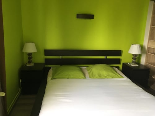 Chambre moderne à La Ferme Du Grand Air avec murs vert citron, lit à structure noire, literie blanche et oreillers verts