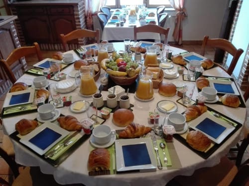 Table de petit-déjeuner élégante à La Ferme Du Grand Air B&B à Fiennes avec viennoiseries, fruits, jus et couverts.