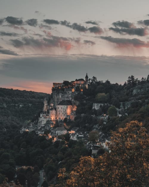 Neuschwanstein Castle perched on cliff at dusk with golden lights and forested valleys below