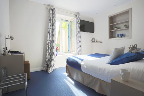 Camera Superiore luminosa presso l'Hôtel De La Fontaine a Nizza con letti gemelli, moquette blu, vista sul giardino, TV e arredamenti moderni