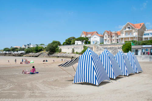 Tentes de plage rayées bleues sur le sable avec villas victoriennes surplombant la plage de La Rochelle